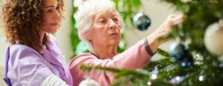 A nursing home resident hangs an ornament on a Christmas tree
