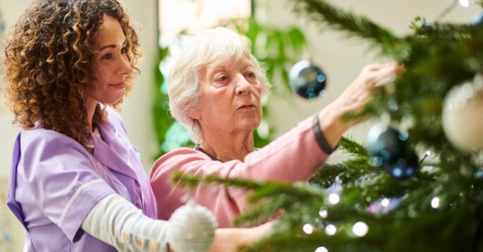 A nursing home resident hangs an ornament on a Christmas tree