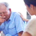 An older man in visible distress is comforted by a caregiver in a nursing home.