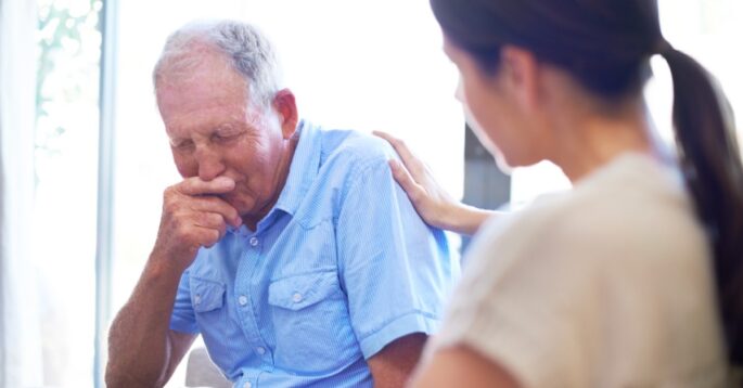 An older man in visible distress is comforted by a caregiver in a nursing home.