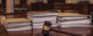 Stacks of legal documents sit on a courtroom table beside a judge's gavel.