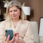 A woman sits on a couch using a smartphone.
