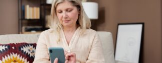 A woman sits on a couch using a smartphone.