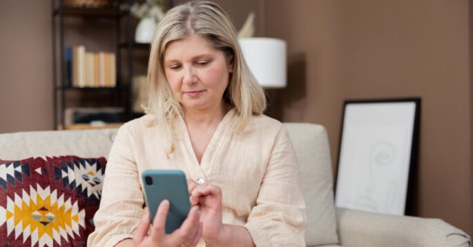 A woman sits on a couch using a smartphone.