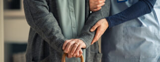 A caregiver supports an older adult using a cane in a nursing home.